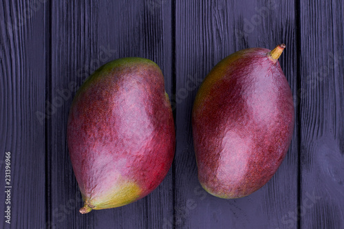 Two organic mango on wooden background. Close up whole fresh mango on black wooden boards. photo