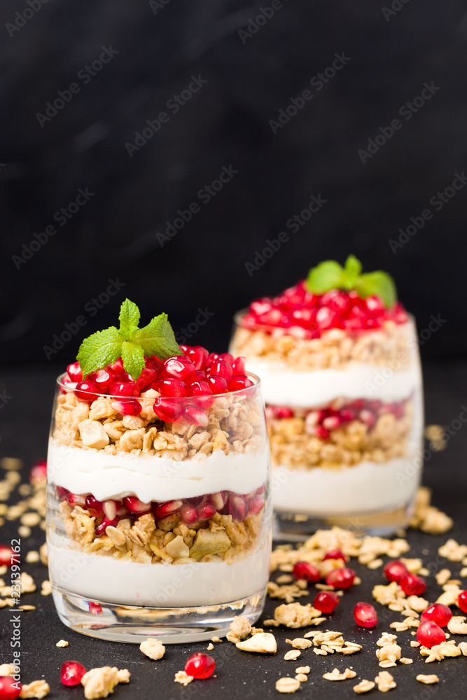 Pomegranate parfait - sweet organic layered dessert with granola flakes, yogurt and fruit seeds on black background. Pomegranate parfait - sweet organic layered dessert with granola flakes, yogurt and fruit seeds on black background.
