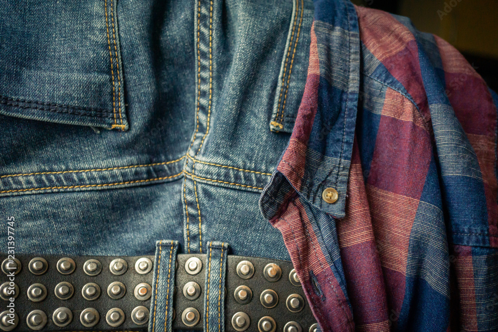 leather belt on a faded pair of blue jeans and details of red and blue checkered shirt