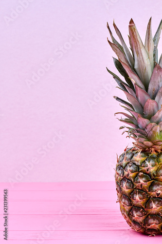 Whole fresh pineapple and copy space. Green organic ananas on pink wooden background and text space, cropped image.