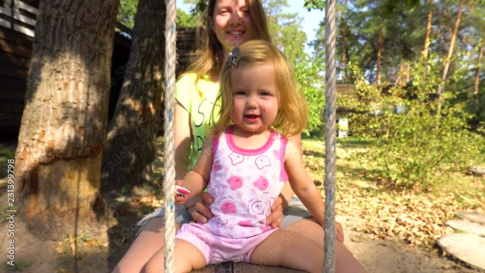 Mother with girl on wooden swing under tree Mother with girl on wooden swing under tree
