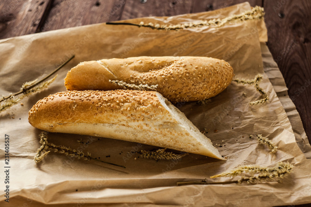 French baguettes with sesame seed on a paper bag lie on a wooden table.
