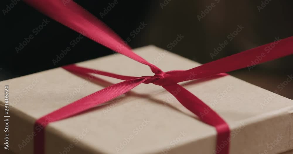 Slow motion macro shot of young female hands opens craft paper gift box with red ribbon bow