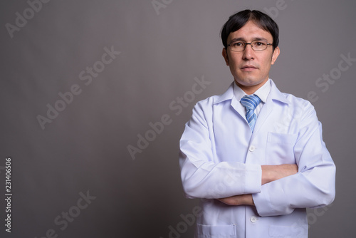 Young Asian man doctor wearing eyeglasses against gray backgroun