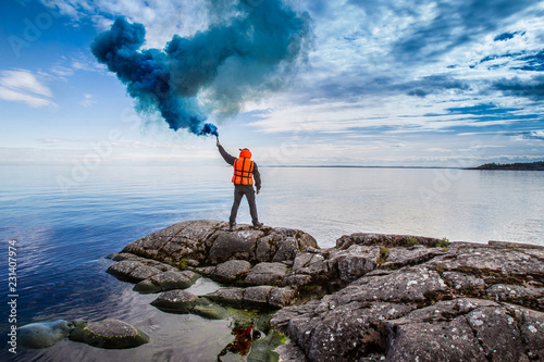 Saving people. The man calls the rescuers. SOS. A man with a smoke bomb. A man in a life jacket. Signal for help. photo