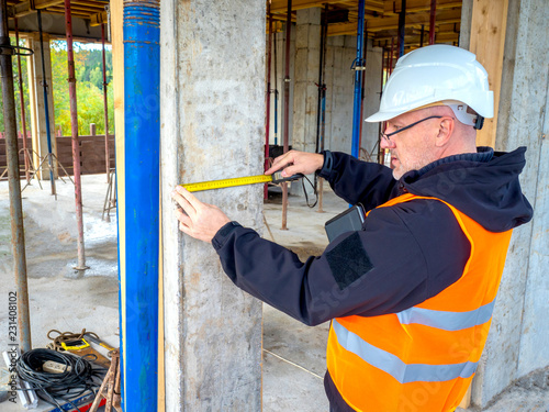 Builder. Engineer builder checks dimensions. A man in a white construction helmet. Construction of the building. A man makes measurements on a construction site.