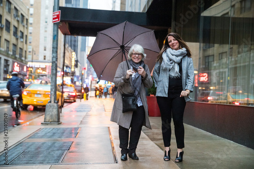 Canvas Print Two happy women together on New York City sidewalk in the rain