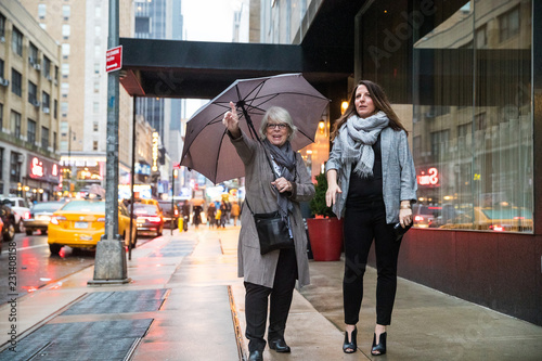 Two women hailing taxi cab in New York on a rainy day while holding an umbrella