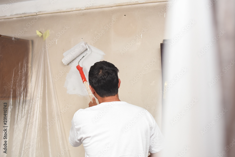 Man painting wall at home with painting roller. Repair home concept. Worker with paint on him after painting dirty walls Man painting wall at home with painting roller. Repair home concept. Worker with paint on him after painting dirty walls
