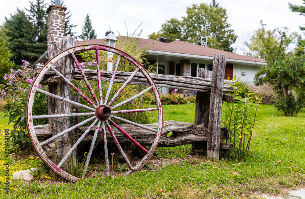 Old antique wagon wheel proped against a rustic fence in Quebec, Canada.