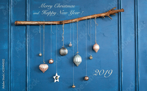 Christmas and New Year greeting card. Beautiful, designer decoration with Christmas balls on a wooden branch against the background of a blue wall in the style of hyuge with stylish inscriptions photo