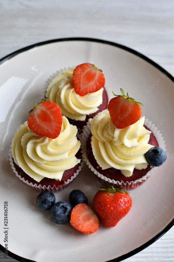 Delicious plate of cupcakes with berries on white wooden surface. Red velvet cupcakes. Delicious plate of cupcakes with berries on white wooden surface. Red velvet cupcakes.