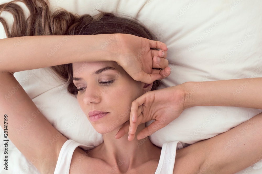 Young woman lying in bed with hand on head Young woman lying in bed with hand on head