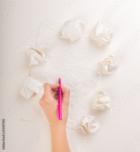 Female hand trying to write next to a few crumpled paper balls 