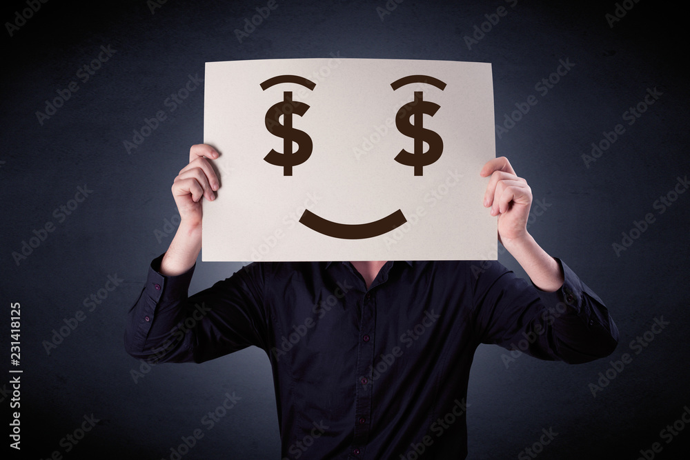 Young casual businessman hiding behind a greedy face drawing on cardboard Young casual businessman hiding behind a greedy face drawing on cardboard