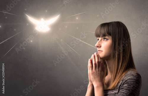 Young woman praying on a grey background with a sparkling bird above her