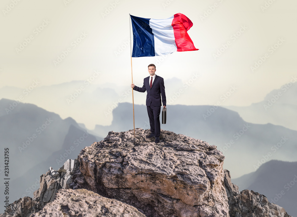 Obraz premium Successful businessman on the top of a mountain holding France victory flag 