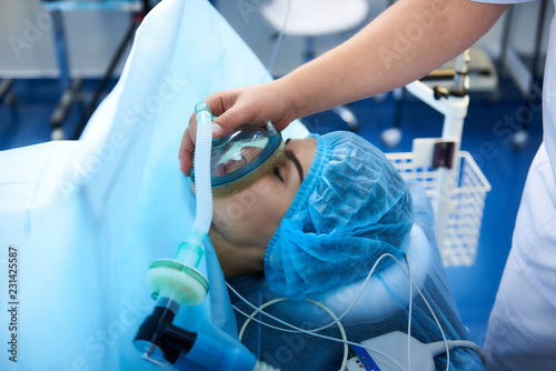 Necessary procedure. Close up of young patient lying with her eyes closed in the operation room and getting narcosis before the surgery photo