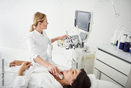 Portrait of beautiful lady in white bathrobe lying on daybed while physician checking results of medical examination