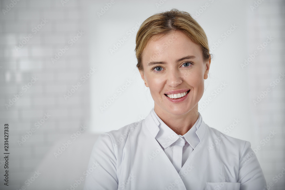 Welcome to our beauty salon. Portrait of young cosmetologist in white lab coat looking at camera with smile Welcome to our beauty salon. Portrait of young cosmetologist in white lab coat looking at camera with smile