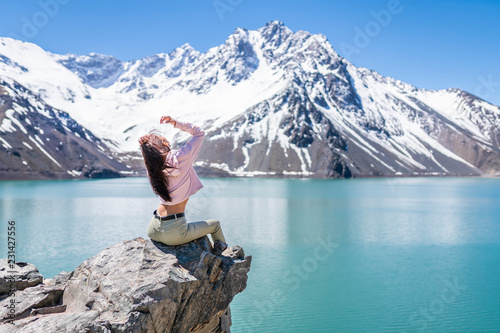 Girl looking at the amazing mountain views of the turquoise waters from the "Embalse del Yeso" (Cast Lake) close to Santiago de Chile city in Andes mountains. Snow mountains and water reflections 