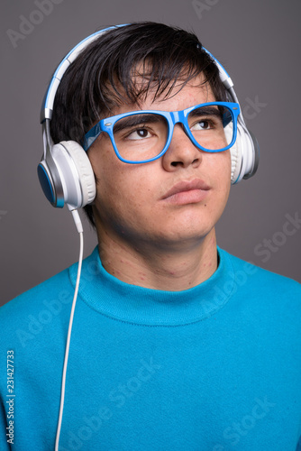 Young Asian teenage boy listening to music against gray backgrou