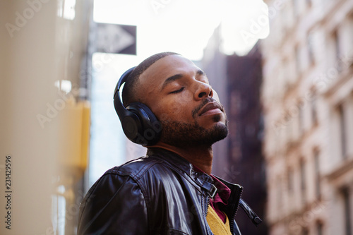Portrait of a young man enjoying listening with his headphones and eyes closed outside on the street