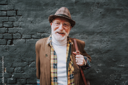 Waist up portrait of joyful hipster pensioner posing near black wall outdoor and happy smiling