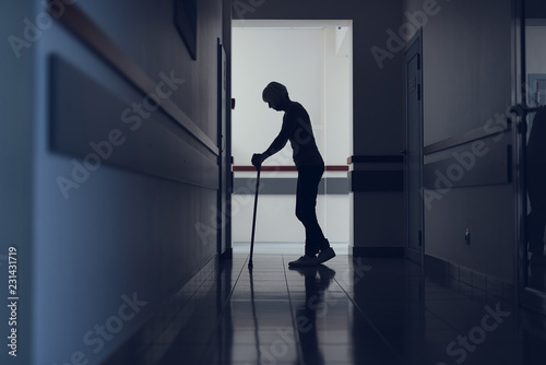 Lady is standing in hospital corridor. She is using cane for walking. Copy space in left side