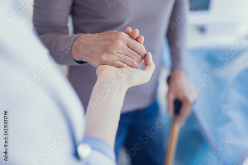 Focus on top view close-up of medical worker supporting woman. Patient is using crutch and leaning on physician arm while they are connecting palms