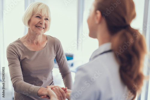 Tela Focus on smiling lady shaking hands with physician after visit to clinic