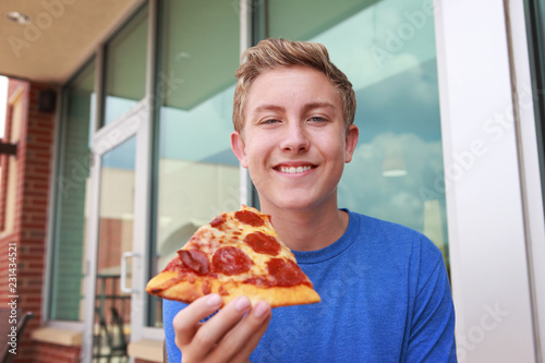 Image of a smiling boy holding a piece of pepperoni pizza