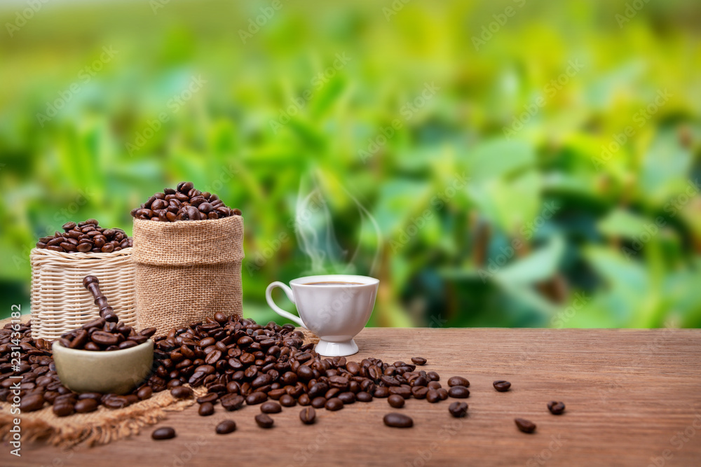Hot cup of coffee and beans with burlap sack on the wooden table, with coffee plantations background. copy space Hot cup of coffee and beans with burlap sack on the wooden table, with coffee plantations background. copy space