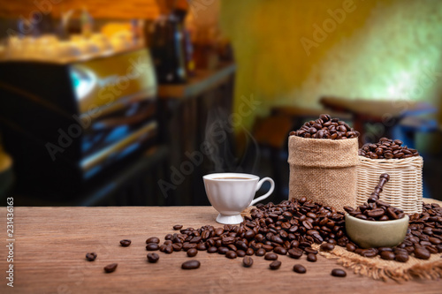 Hot cup of coffee and beans with burlap sack on the wooden table, with coffee shop background. copy space