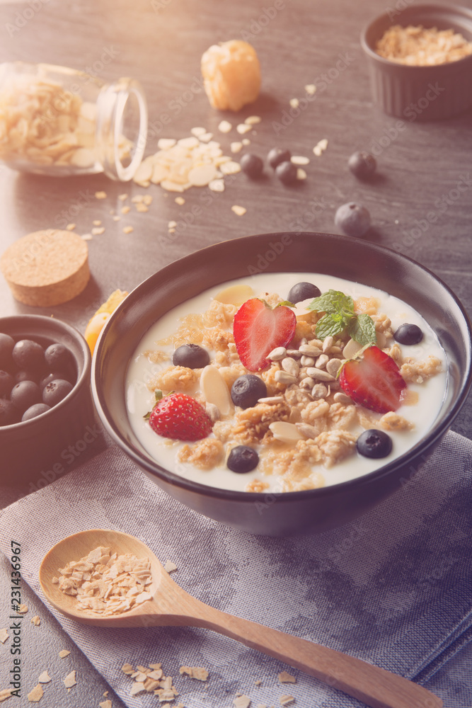 bowl of oat granola with yogurt, fresh strawberry, blueberries and nuts on black wooden table