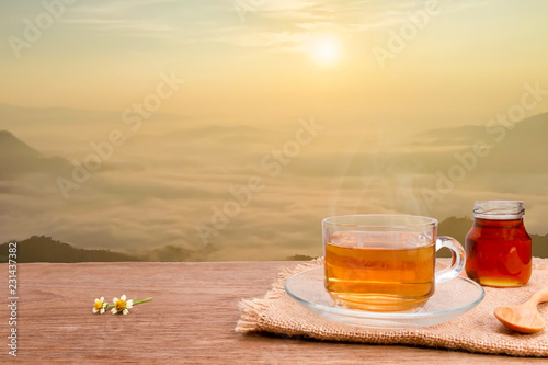 Hot tea cup and honey on the wooden table with Sunrise with mist on high mountain in the morning. Healthy drink with copy space
