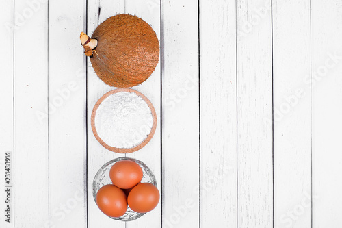 Eggs, flour and coconut on white table photo