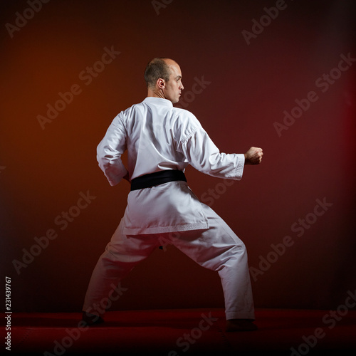 On a dark background, an athlete with a black belt does formal karate exercises