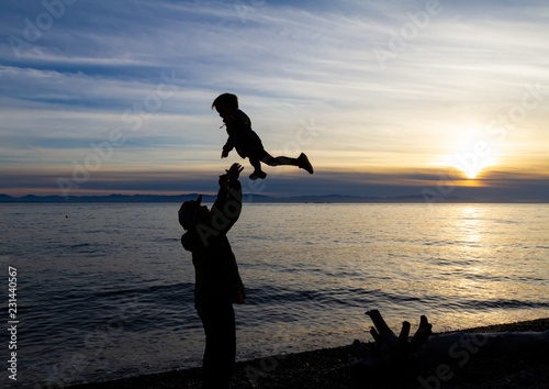 Parent playing with his son the beach at the end of day at sunset in the background