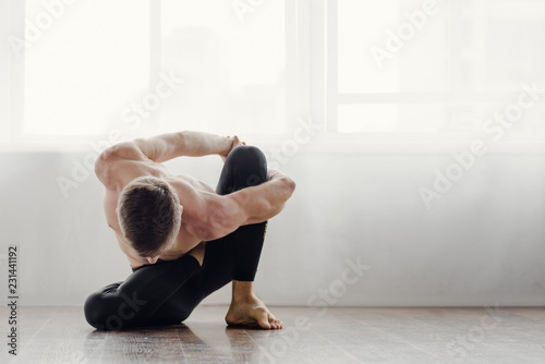 Athletic muscular young man practicing yoga in studio
