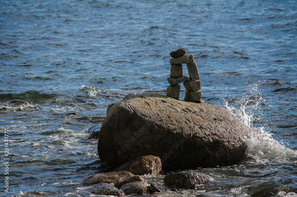 Fototapeta premium Water splashing up on an Inuksuk in Stanley Park's English Bay, Vancouver, BC, Canada
