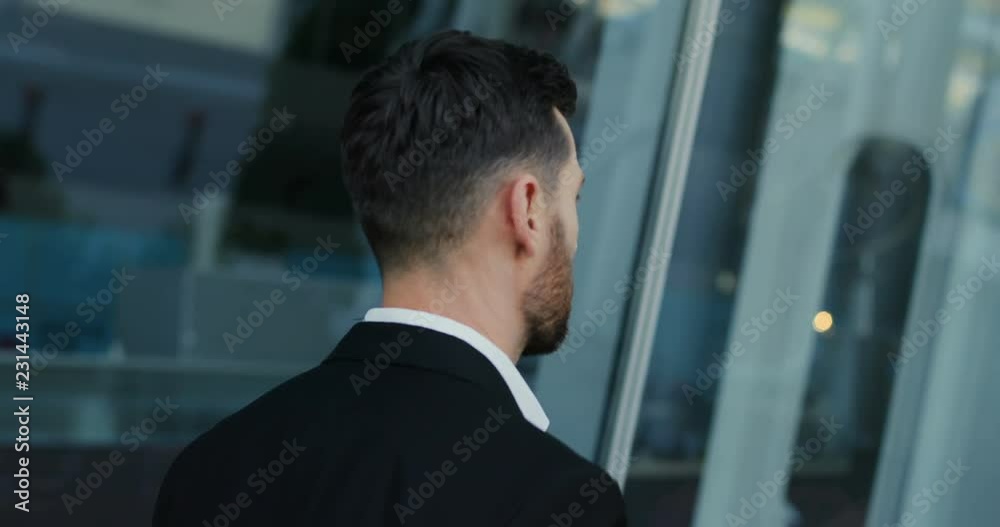 Close up of the back view of the man in the suit walking at the airport ot other station on the street with his wheeling suitcase. Rear. Close up of the back view of the man in the suit walking at the airport ot other station on the street with his wheeling suitcase. Rear.