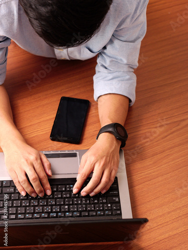 Wallpaper Mural Closeup of a man laying typing on laptop wearing smart-watch and mobilephone beside. Torontodigital.ca