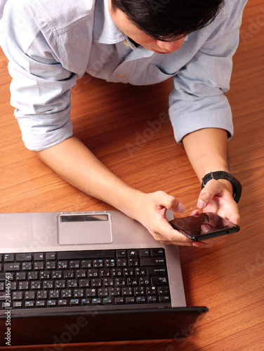 Wallpaper Mural Closeup of a man laying typing on mobilephone wearing smart-watch and laptop beside. Torontodigital.ca