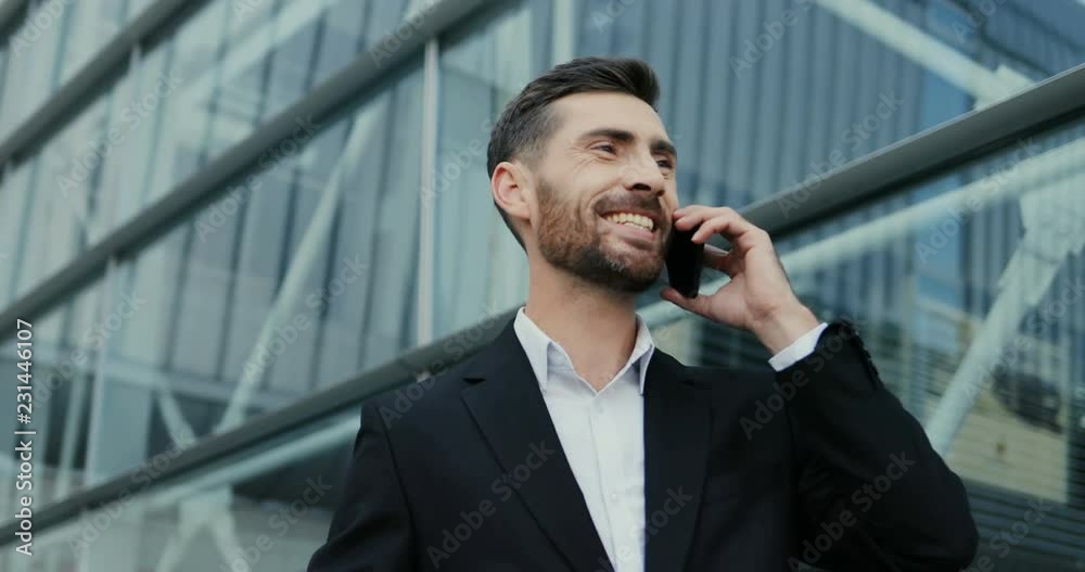 Portrait of the handsome smiled Caucasian businessman talking on the phone cheerfully and doing yes gesture with a hand. Close up. Outdoor. Portrait of the handsome smiled Caucasian businessman talking on the phone cheerfully and doing yes gesture with a hand. Close up. Outdoor.