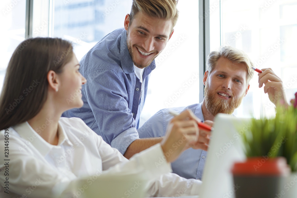 Group of young modern people in smart casual wear pointing at laptop and smiling while sitting in the office. Group of young modern people in smart casual wear pointing at laptop and smiling while sitting in the office.