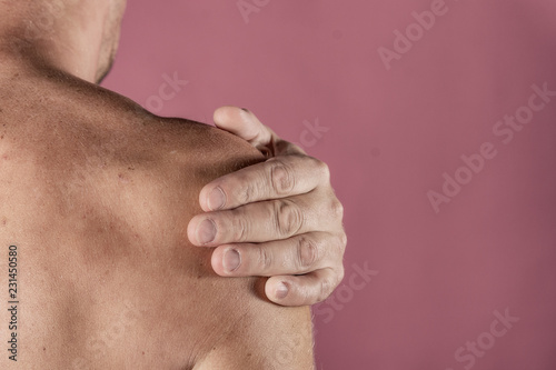 Man holding his sore shoulder trying to relieve pain on pink background. Health problems