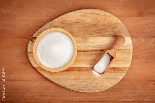 An overhead photo of a bowl and a scoop of white sugar, shot from the top on a dark rustic wooden background with copy space