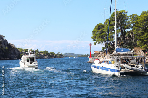 Sailing catamaran sails along the rocky green coast past the red literary sign - the fairway lighthouse. City of Sibenik in the Dalmatia region in Croatia. Adriatic sea in the Mediterranean area.