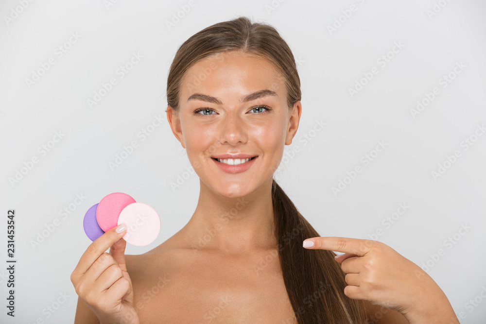 Beauty portrait of pleased shirtless woman with long brown hair smiling and holding colorful cosmetic pads, isolated over white background Beauty portrait of pleased shirtless woman with long brown hair smiling and holding colorful cosmetic pads, isolated over white background